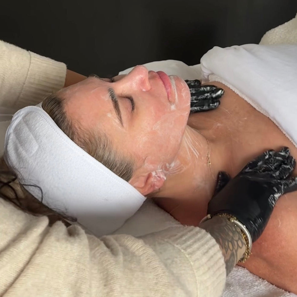 Person receiving a facial treatment with a white towel and black gloves.