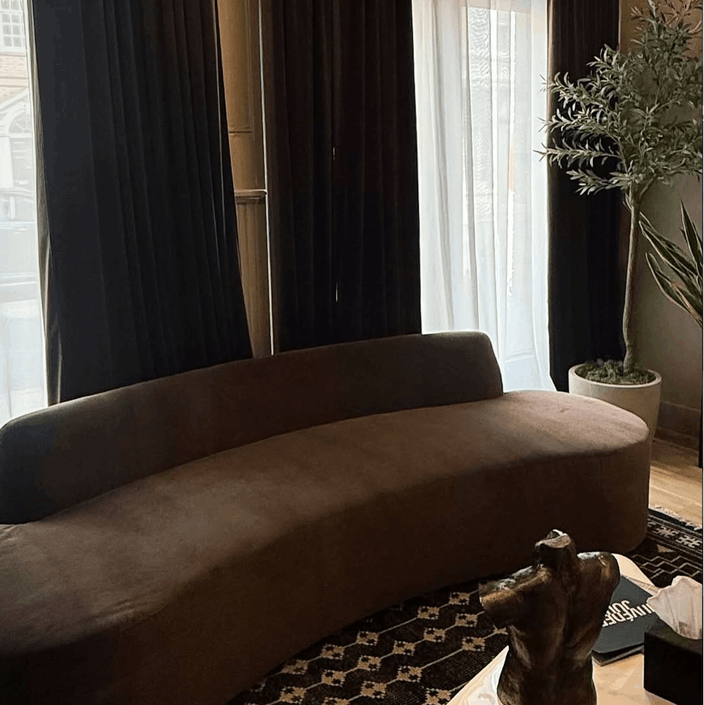 Brown curved sofa in a room with dark curtains and a patterned rug at the best med spa in philadelphia.