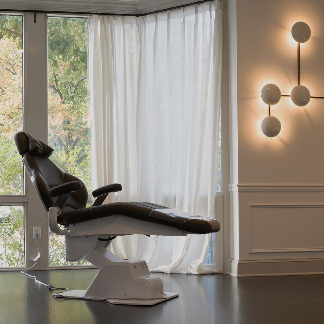 Modern massage chair in a room with large windows and decorative wall lights.